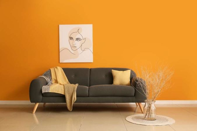 Un canapé confortable de couleur grise mis en valeur devant un mur orange vif dans un salon moderne.