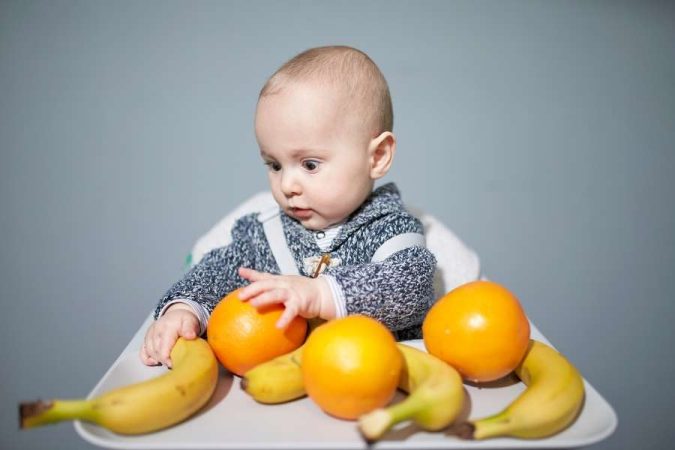 Un bébé explore des fruits entiers sur son plateau lors d'une session de diversification menée par l'enfant.