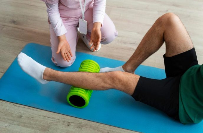 Un sportif effectue un massage ischios-jambiers avec un rouleau de massage vert sous la supervision d'une professionnelle.